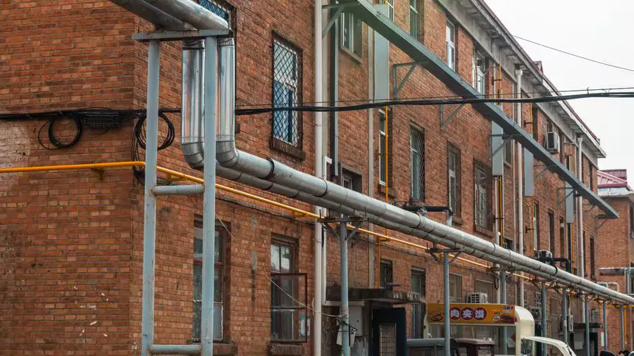 Exterior view of brick building with exposed industrial pipes and utility lines.